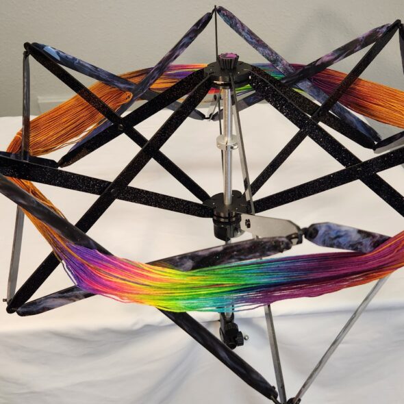 Alpenglow Glider Swift in Deep Space—black glitter frame with galaxy-marbled accents, yarn on the swift.